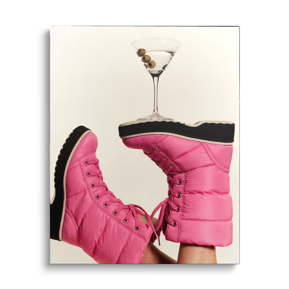 Toile Après-Ski vue de face sur fond blanc : photographie de jambes en bottes de neige matelassées roses, un verre de martini en équilibre sur une semelle