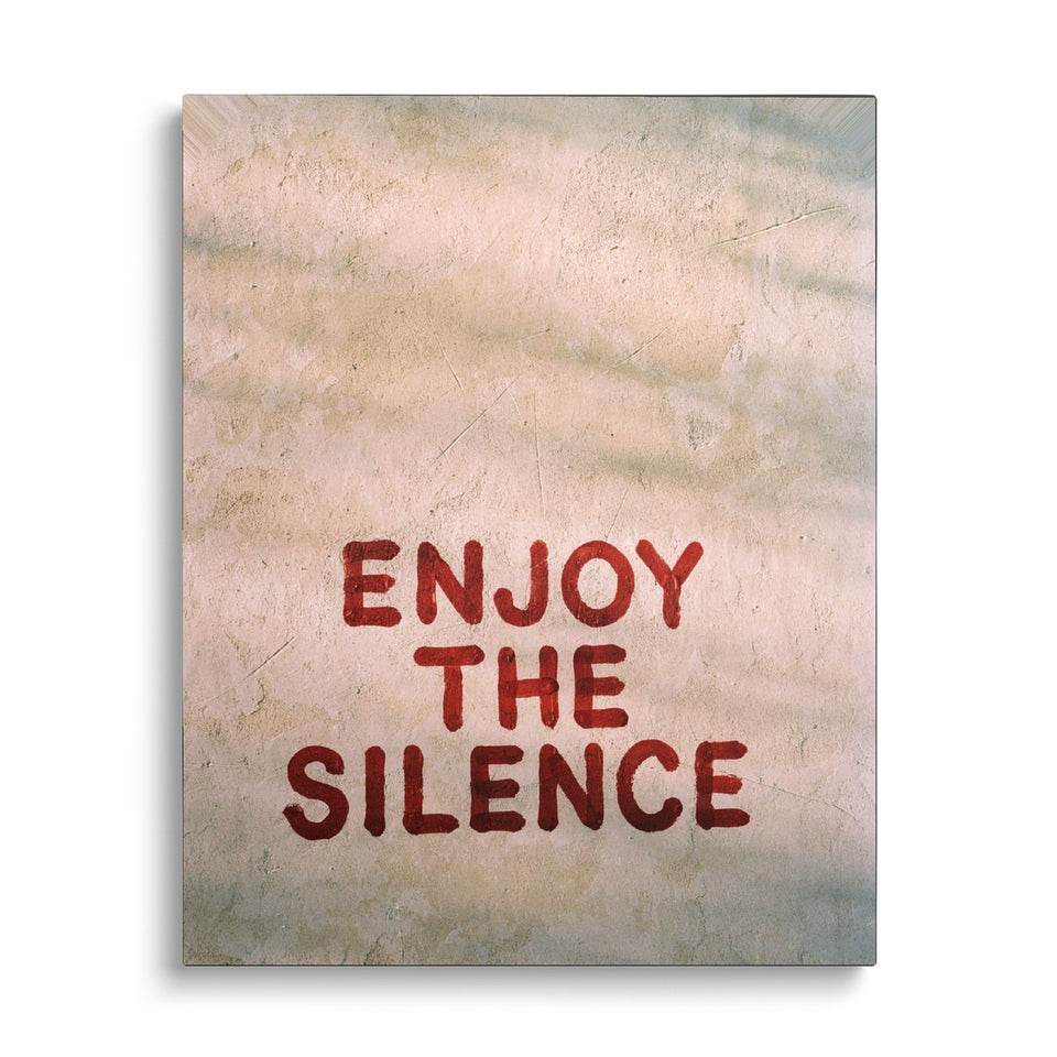 Toile Enjoy the Silence vue de face sur fond blanc : mots « Enjoy the silence » peints en lettres rouges au bas d’un mur d’enduit beige