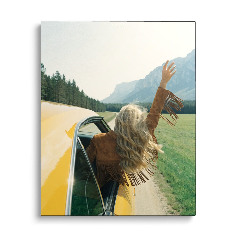 Toile Free vue de face sur fond blanc : photographie d’une femme blonde en veste à franges penchée à la fenêtre d’une voiture jaune, bras levé, face aux montagnes