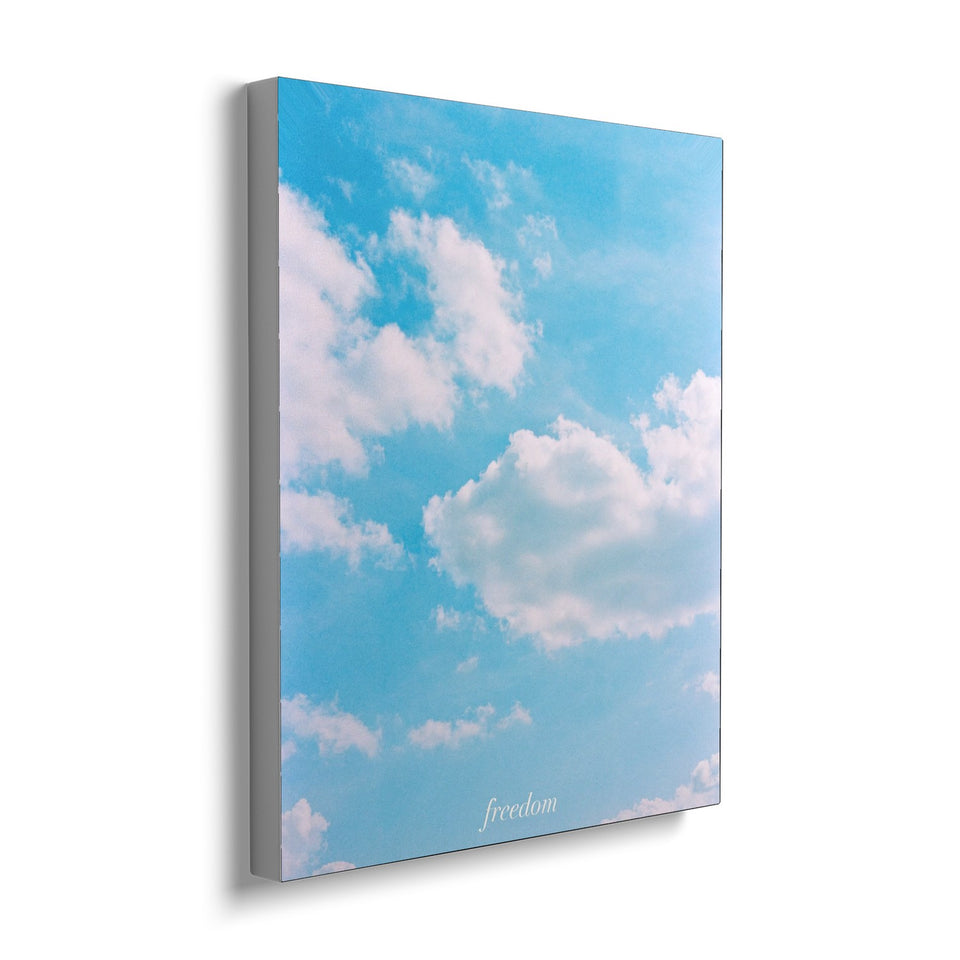 Toile Freedom 40 × 50 cm, vue de trois quarts avec tranche blanche : photographie d’un ciel bleu semé de nuages blancs, avec le mot « freedom » en petites lettres