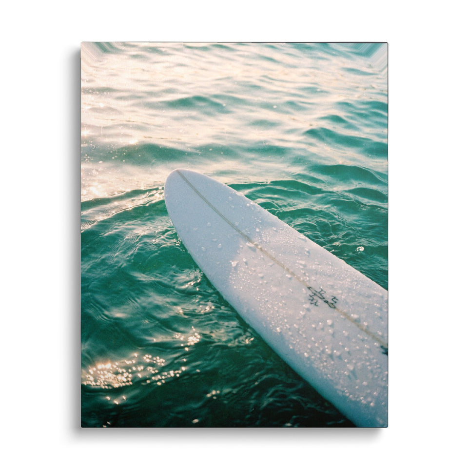 Toile Glisse vue de face sur fond blanc : photographie d’une planche de surf blanche perlée de gouttes, posée sur une eau vert émeraude