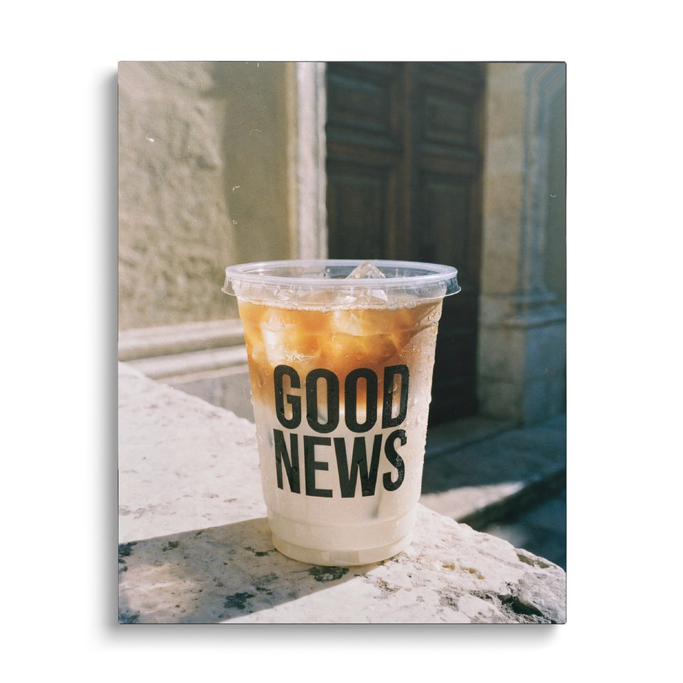 Toile Good News vue de face sur fond blanc : photographie d’un café glacé posé sur un muret de pierre au soleil, le gobelet marqué « Good news »