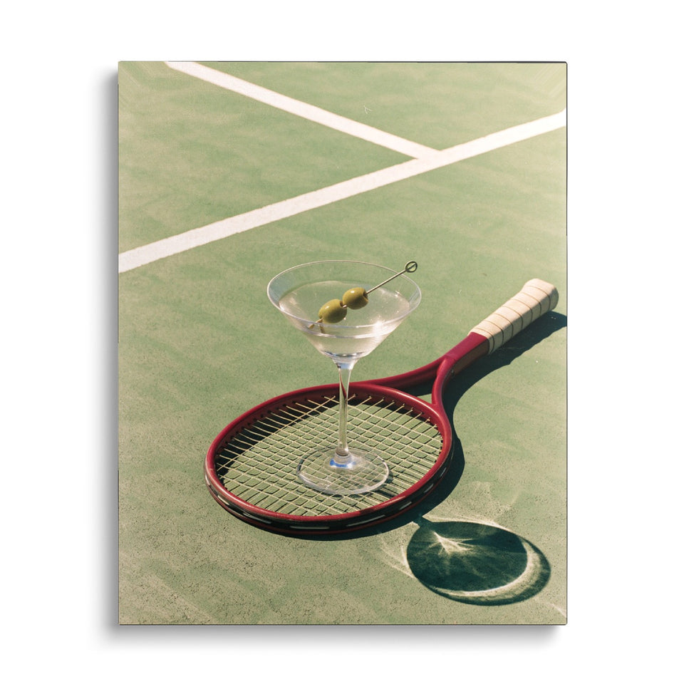 Toile Jeu, Set et Martini vue de face sur fond blanc : photographie d’un verre de martini aux olives posé sur une raquette de tennis, sur un court vert