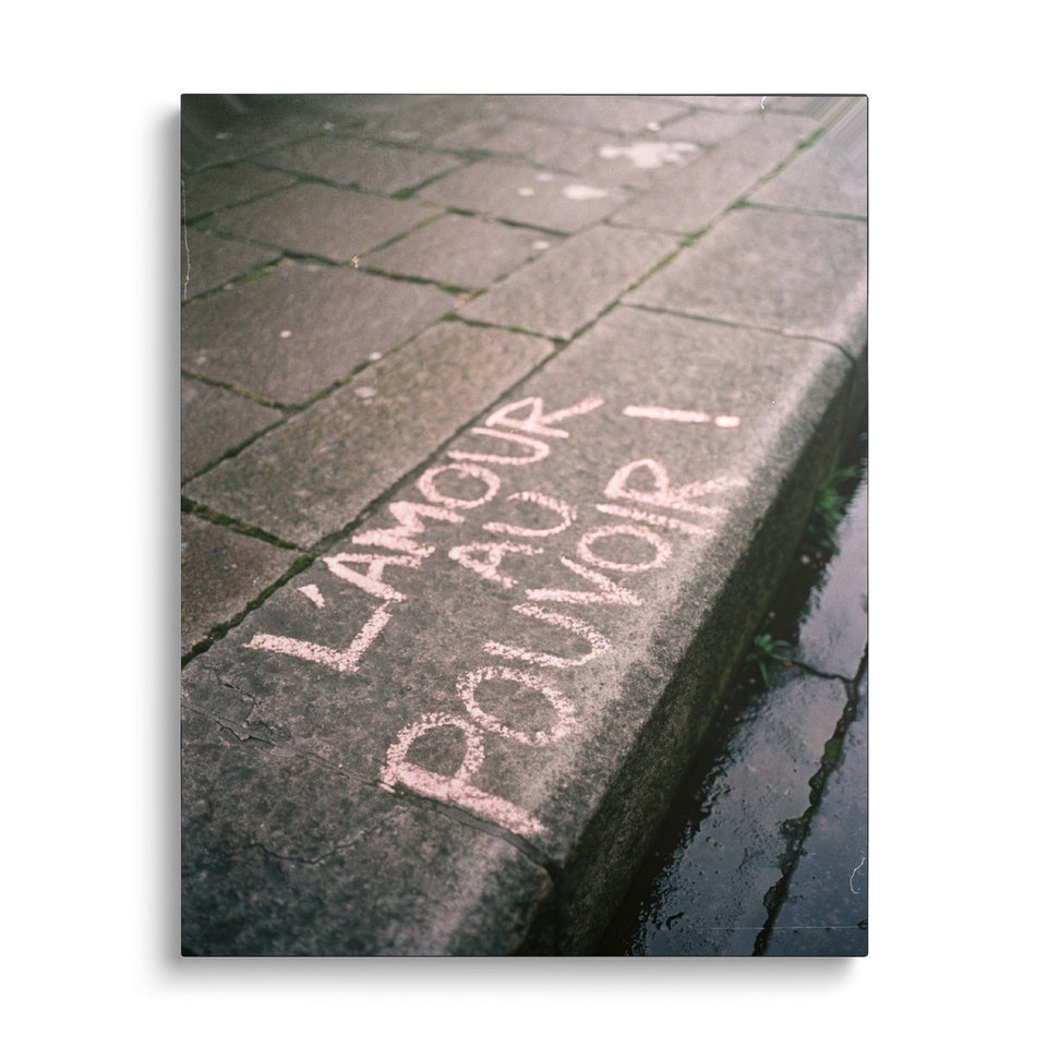 Toile L’Amour au Pouvoir vue de face sur fond blanc : photographie d’un trottoir pavé où est écrit à la craie rose « L’amour au pouvoir ! »