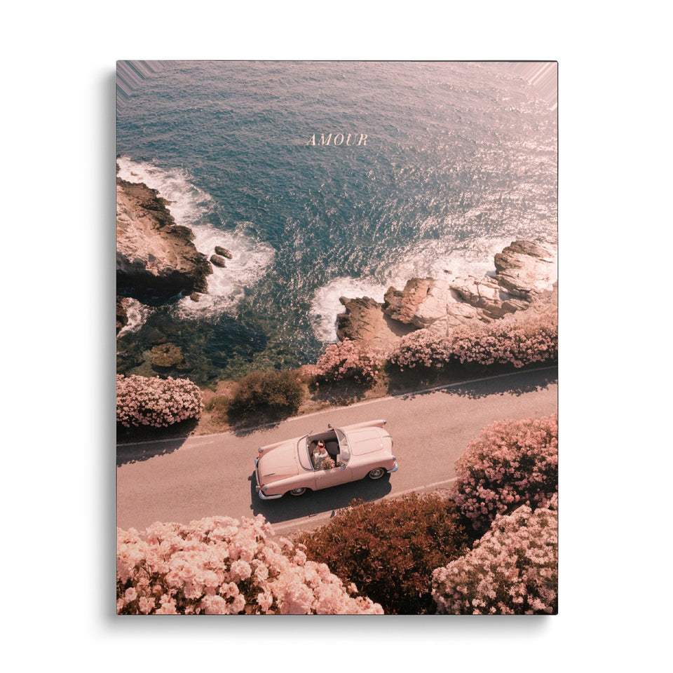 Toile La Corniche vue de face sur fond blanc : photographie aérienne d’un cabriolet rose sur une route de bord de mer bordée de massifs de fleurs roses