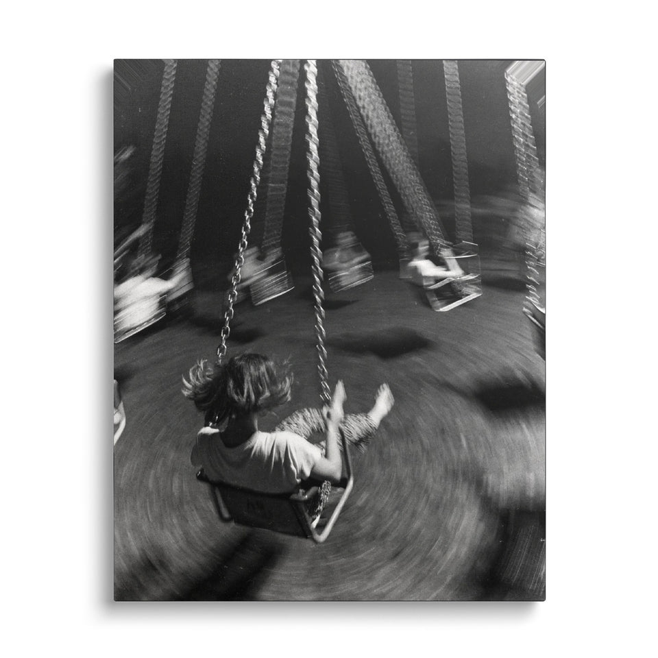 Toile Le Manège vue de face sur fond blanc : photographie noir et blanc d’un enfant sur un manège de chaises volantes, en plein mouvement