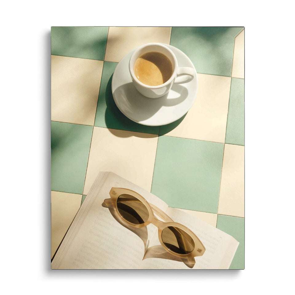 Toile Pause Soleil vue de face sur fond blanc : photographie d’un expresso, de lunettes de soleil et d’un livre ouvert sur une table à damier vert et crème