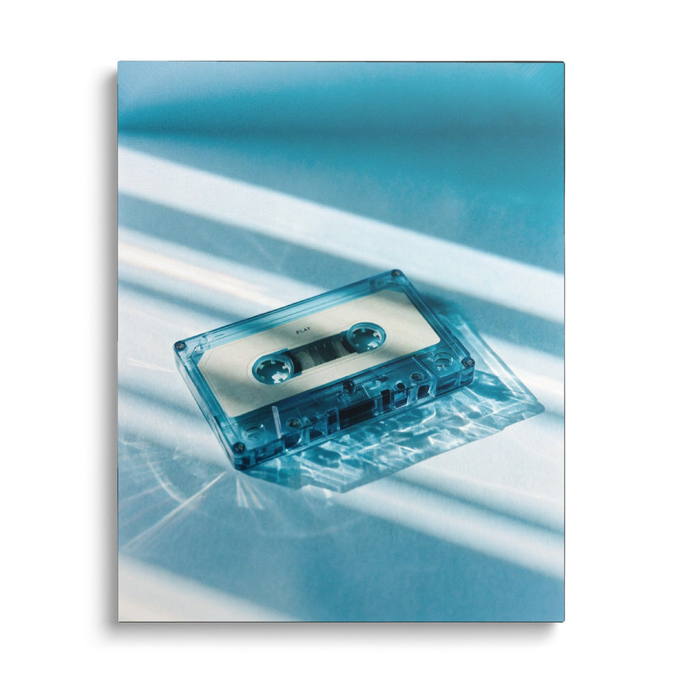 Toile Play vue de face sur fond blanc : photographie d’une cassette audio transparente bleutée posée dans des reflets de lumière