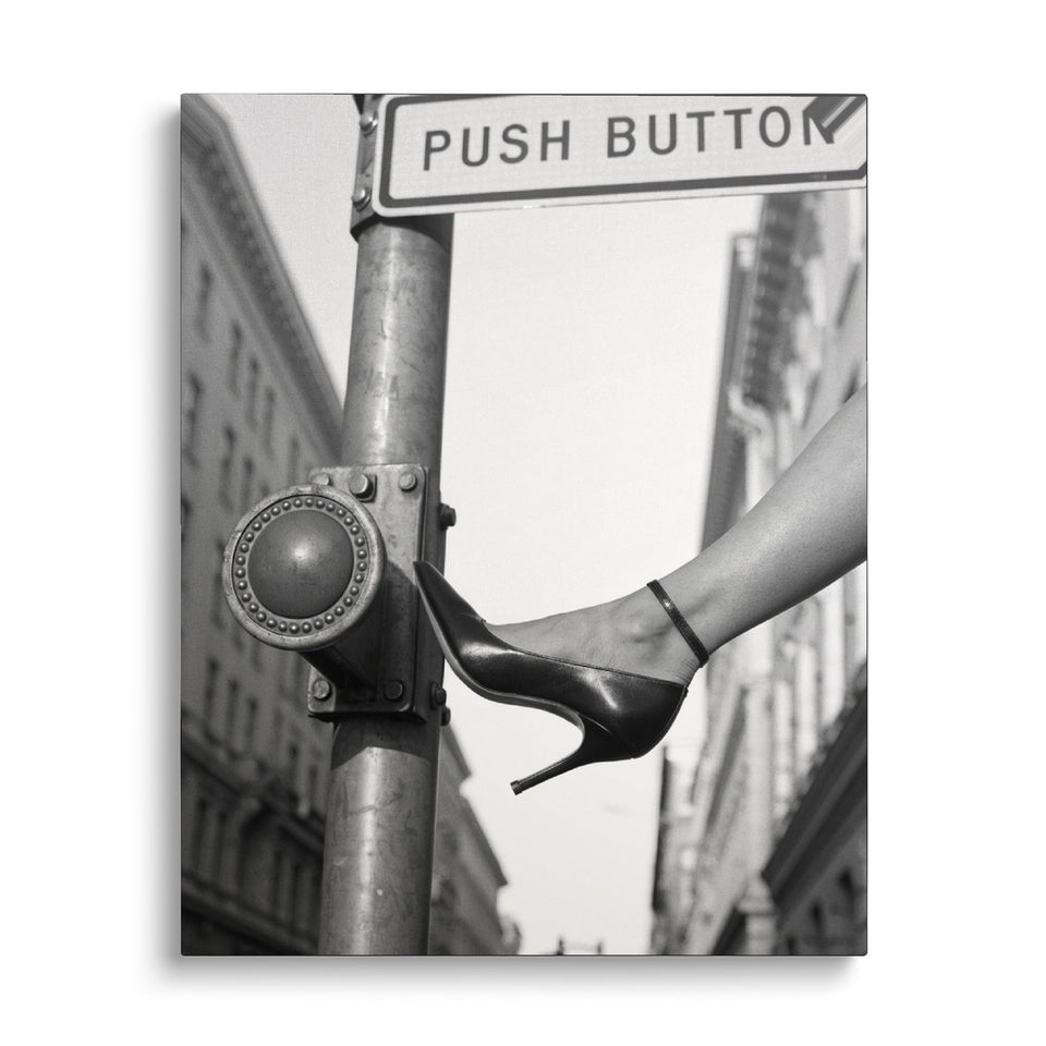 Toile Push Button vue de face sur fond blanc : photographie noir et blanc d’un escarpin à talon aiguille appuyant sur un bouton de passage piéton « Push button »