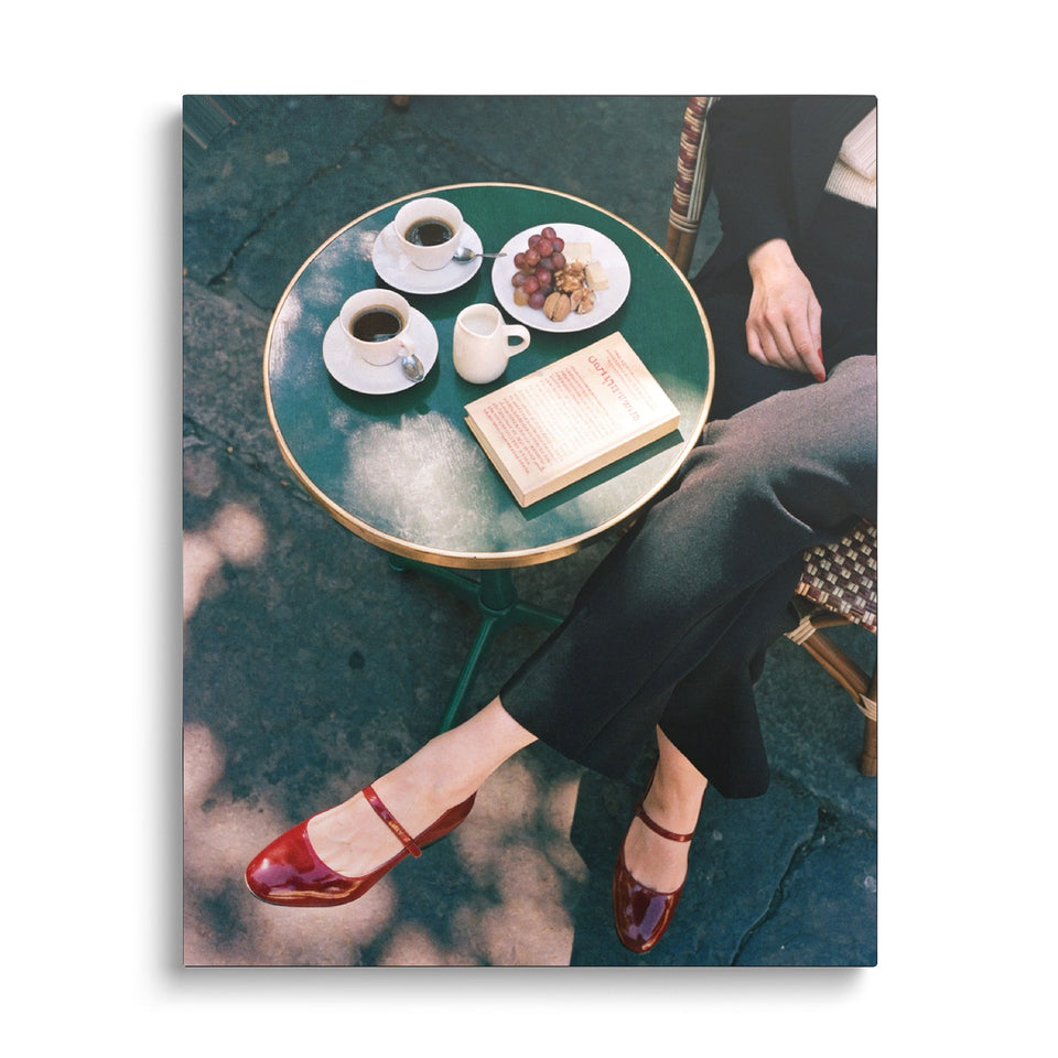 Toile Table pour Une vue de face sur fond blanc : photographie vue du dessus d’un guéridon vert avec deux cafés, des fruits et un livre, jambes croisées en babies rouges