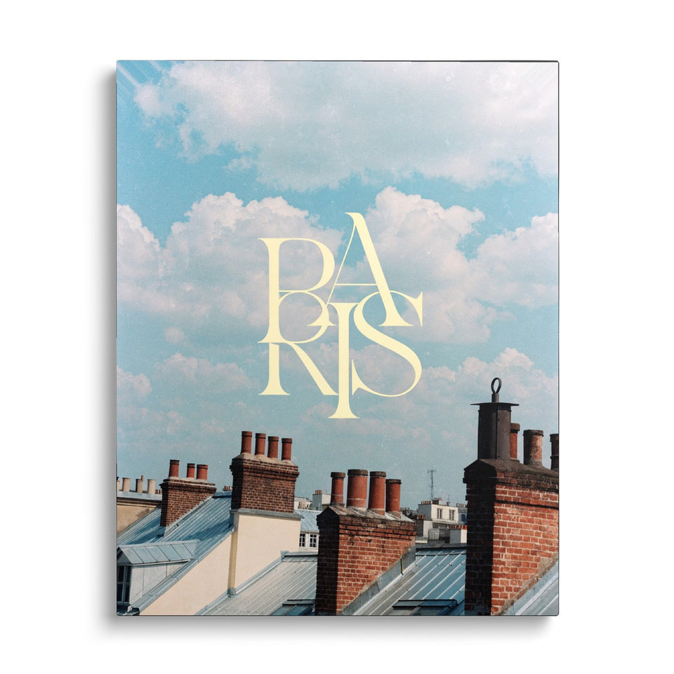 Toile Toits de Paris vue de face sur fond blanc : photographie de toits et de cheminées parisiens sous un ciel de nuages, avec le mot « Paris » en lettres crème entrelacées
